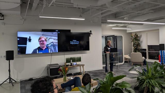 Cameron Dutro giving a talk, behind them two zmtv monitors, one with the presentation and another with the person face.