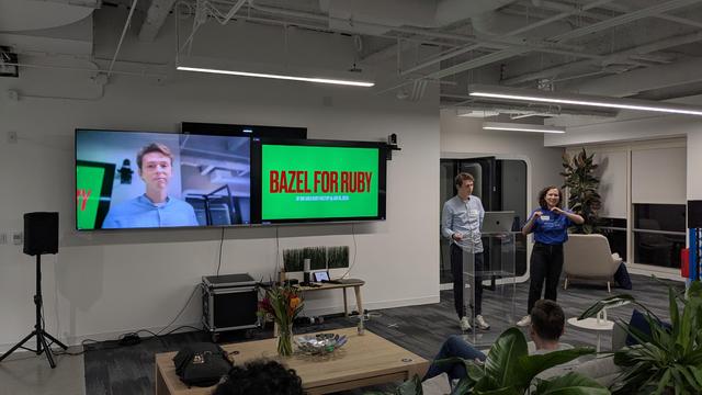 Alex Rodionov presenting in #SFRuby meeting, in their back two TV monitors, one with the presentation and another filming their face.