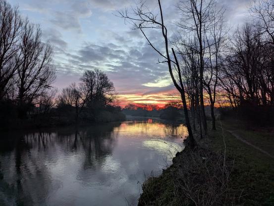Image of a river in the early morning, with the sun rising in the background causing a red set of clouds on the horizon.