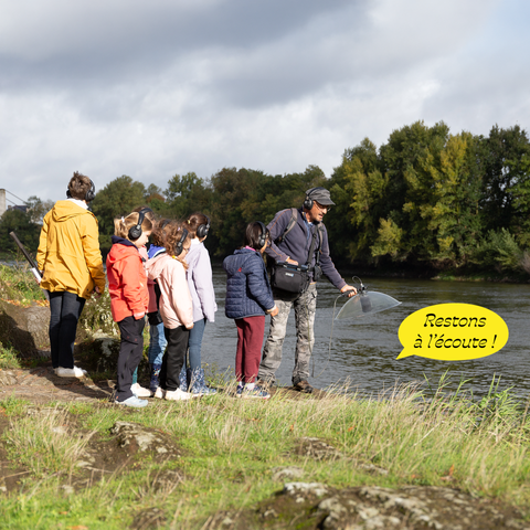 En bord de Loire, un homme tient un micro dans sa main gauche pour faire écouter des sons du fleuve à un groupe d'enfants qui portent un casque sur les oreilles. Une bulle de BD indique que la Loire leur parle et dit : "Restons à l'écoute !"