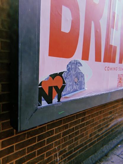 The edge of a billboard. The posters have been torn to reveal a heart shape. underneath. The colours are pink, red, denim blue.