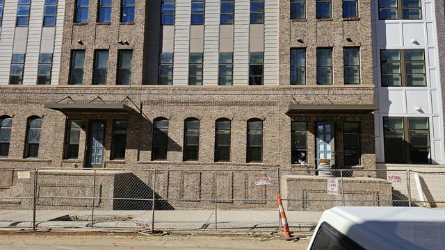 A workers scrapes in the window of the lower level of an upscale apartment complex built into an old brick warehouse. It is surrounded by a fence.
