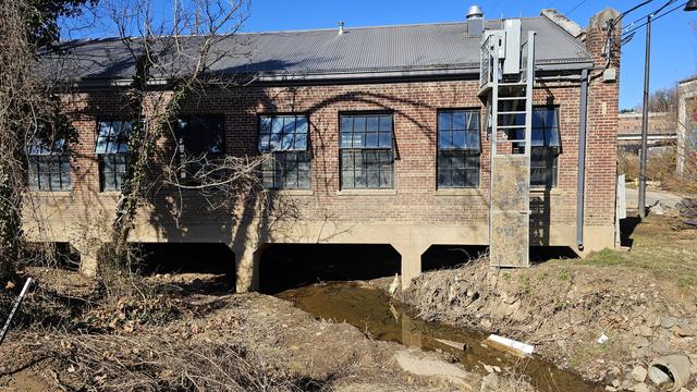 Back of small brick building with a stream running under it. Mudline shows extent of flooding halfway up the building.