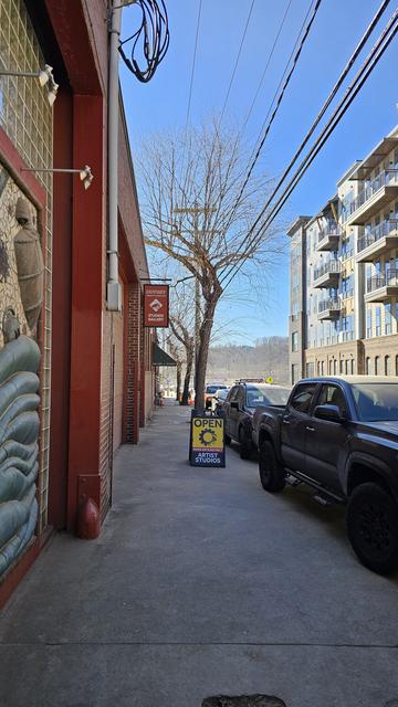 Sidewalk with warehouses on left, parked cars on right. High sign for Odyssey Gallery and sidewalk sign saying Artist Studio Open.