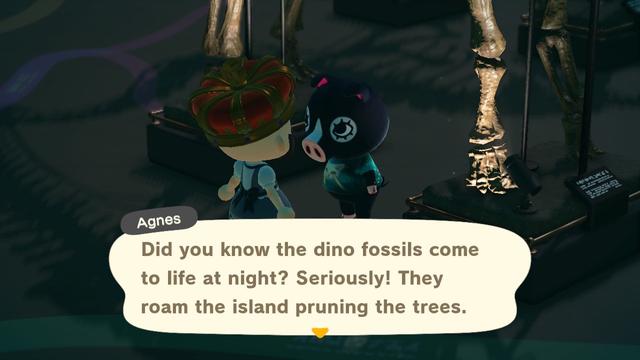 Animal Crossing: New Horizons screenshot. Set in the museum underneath a large dinosaur skeleton. Agnes (black pig wearing a green meme shirt) is talking to a bald human seen from behind wearing a black / grey magical girl dress and an enormous crown. Agnes is saying, "Did you know the dino fossils come to life at night? Seriously! They roam the island pruning the trees."