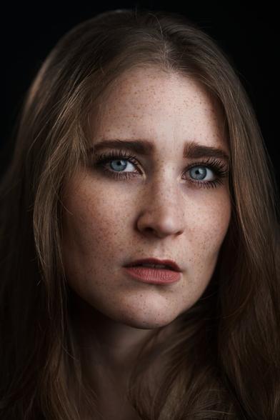 Portrait einer braunhaarigen Frau mit blauen Augen. Sie schaut in die Kamera.