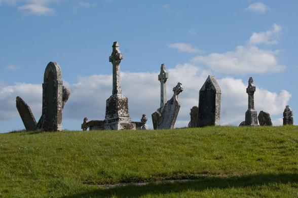 A series of tombs in a grass field with a blue sky.