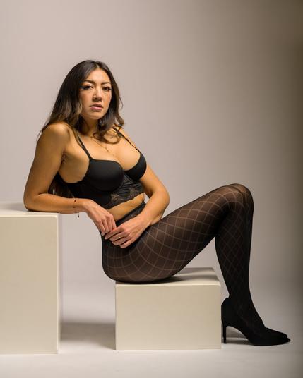 Eine Frau sitzt auf weißen Würfeln in einem Fotostudio mit weißem Hintergrund. Sie trägt elegante Unterwäsche von Victoria's Secrets und wirkt selbstbewusst und elegant. Das Studio ist minimalistisch, mit einem klaren und sauberen Setup, das den Fokus auf sie lenkt.