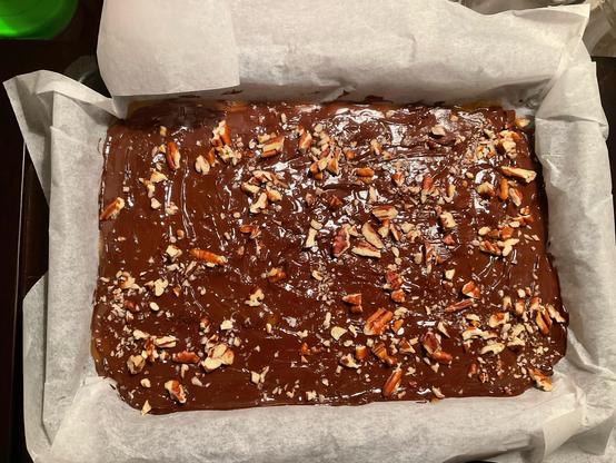 Baking tray full of toffee covered in chocolate and chopped pecans.