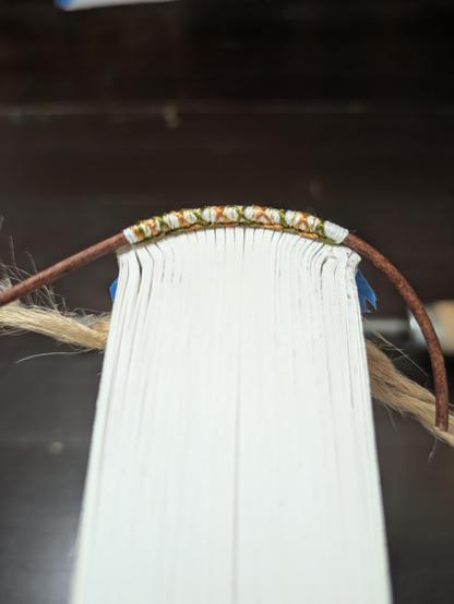 The top edge of a book showing the hand sewn endband that is white, green, and gold.