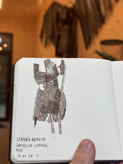 Drawing of a leather armor done in brown ink. Sketchbook is held up to include the actual armor in the back.