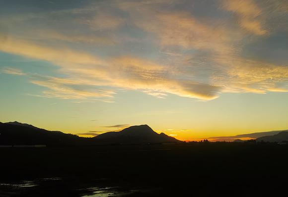 Sunset over silhouetted mountains. The sky is filled with wispy, golden clouds.