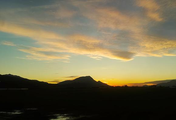 Sunset over silhouetted mountains. The sky is filled with wispy, golden clouds.