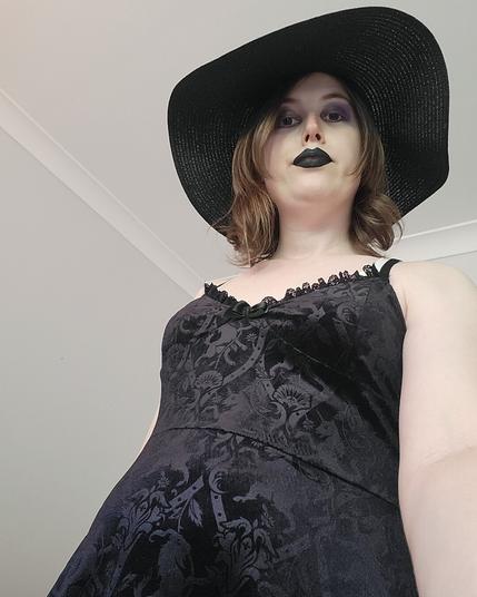 Selfie of Revy from a low up angle
She's completely goth with eye shadow & black lipstick and a big black brim hat and a goth dress too