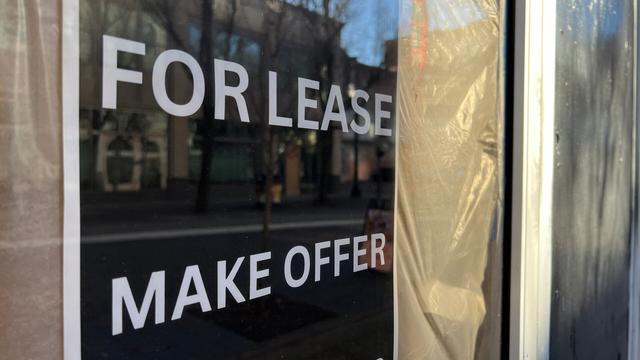 close up of a 'for lease' / 'make offer'  sign on a glass door, with taped plastic blocking view inside. the building across the street appears as a soft reflection in the glass.