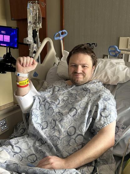 Me, back in my room, still in the gown, after a successful surgery to remove my appendix, laying in a hospital bed. My fist is raised in triumph.