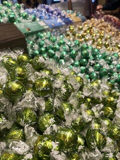 A pile of Linder chocolate truffles wrapped in green foil on display in a store