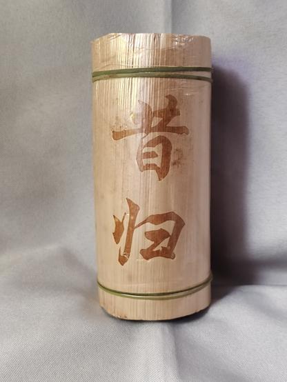 The tea comes packaged like this.  The bamboo cylinder it was compressed and aged in has been removed and the tea is now wrapped in crepe paper and a broad leaf of some kind.  Strips of bamboo have been used as twist ties to hold it all together.

The village name is written in semi-cursive calligraphy on one side.