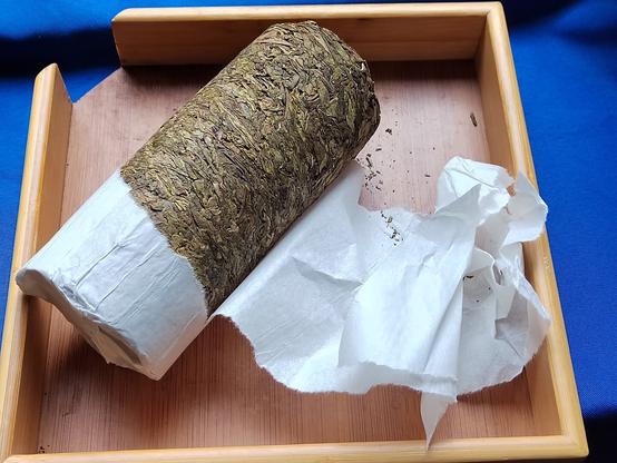 As the white paper is torn off, the strange form factor of the tea is revealed.  Being a very young raw tea, it's still mostly green with only hints of the brown that it will eventually develop if left to age for a few more years.  Even when this tightly compressed, the fact it came from old growth, large-leaf tea is very obvious.