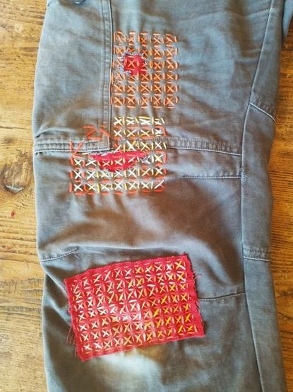 Photo d’une jambe de pantalon de travail qui a été réparé avec des points de broderie Sashiko de couleurs rouge, orange, jaune.