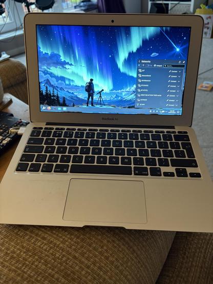 Tiny silver MacBook running a pretty KDE Plasma desktop with WiFi networks showing
