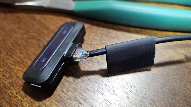 A USB-C wireless microphone receiver with a cable attached to it where the USB-C male plug used to be. The cable enters where the plug used to exit, and is surrounded by a rough blob of hot-glue, an  un-shrunk over-sized short length of heat-shrink sits on the cable just up a bit from the device ready to be slipped over the protruding nub of the device like a very oversized condom.