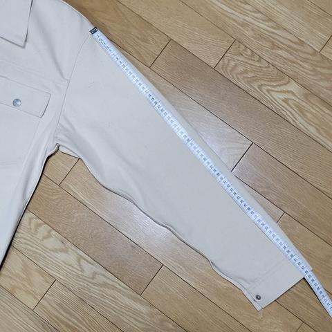 Left sleeve of an off-white sateen jacket with a tape measure along the sleeve
