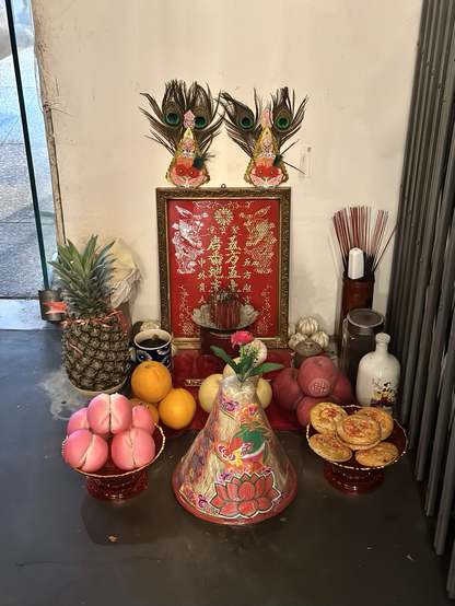 Food offering during chinese new year outside a restaurant with a selection of food, fruit, sweets & incense.
