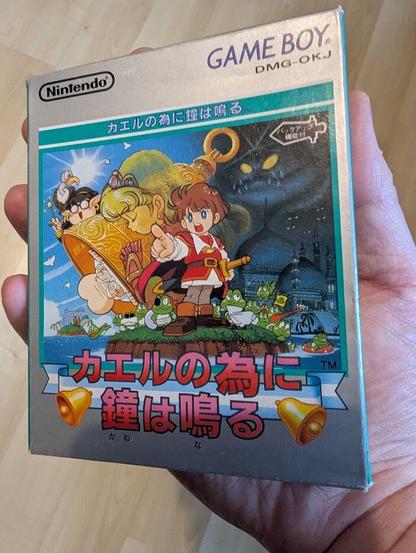 The box art of the game Kaeru no Tame ni Kane wa Naru. The cover art of features a character holding a sword surrounded by frogs and other characters, standing on a small island. In the background, with a castle and full moon in the background, a sunny island environment can be seen on the left and to the right, a dark ominous castle and a dark figure standing above.