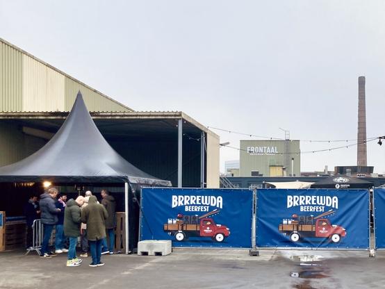 Entrance of the Brrrewda Beerfest in Breda: fences covered with the festival banner, people queuing up for the ticket control, and the Frontaal brewery visible in the background