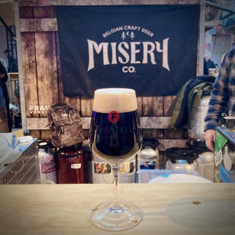 A tasting glass with stout on the bar, a banner of brewery Misery Co. in the background