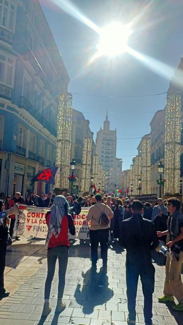 manifestacion de palestina the surge en malaga. calle larios a contraluz con la dilueta de la equitativa y el sol de mediodia en el centro