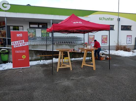 Ein Pavillion mit dem Logo der sozialdemokratischen Partei Österreichs. Links daneben steht ein Rollup mit dem Text SPÖ - Es Lebe der Ort!

Im Pavillion sind eine Heurigenbank und zwei Stehtische aufgebaut. Im Hintergrund richtet eine Person Getränke her