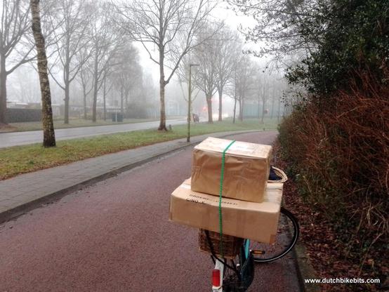 Bicycle on a cyclepath with parcels loaded on the back. The cyclepath also has other cyclists on it. There are cars on the road, spaced from us by a large verge, making it's safe to cycle in fog.