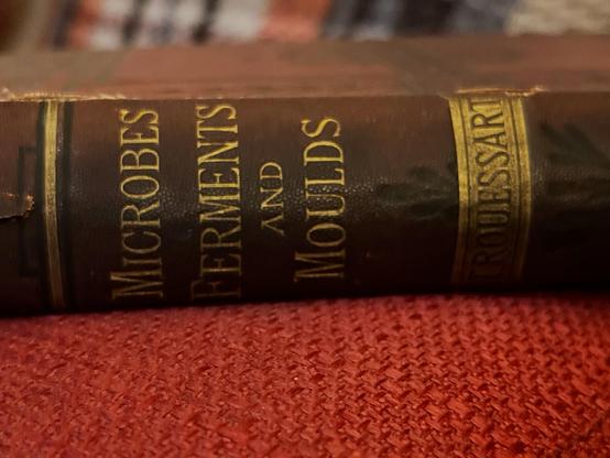 A dark red book with gold letters that read Microbes ferments and moulds.