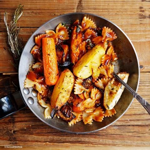 lzuntergrund gemasert. Darauf eine kleine silberne Pfanne. Darin: Farfalle »Alviano« mit geröstetem Ofengemüse und einer Rotwein-Tomatensauce.