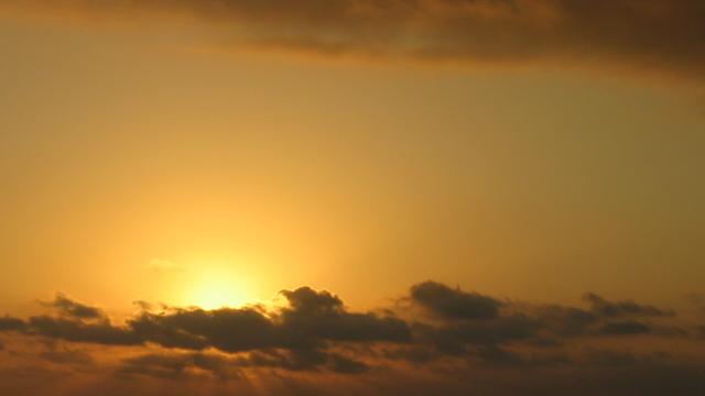 Sun behind clouds in a yellow sunset sky. Photo: Stefan Romero Grieser, CC BY-SA 4.0