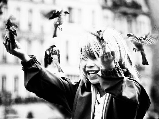 smiling young person with birds fluttering around their fingers