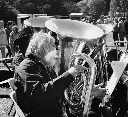 Monochrome. Portrait of a man playing a euphonium taken from the side. The sun is reflected from the instrument onto the lower half of his face creating a sharp demarcation of bright and dark.