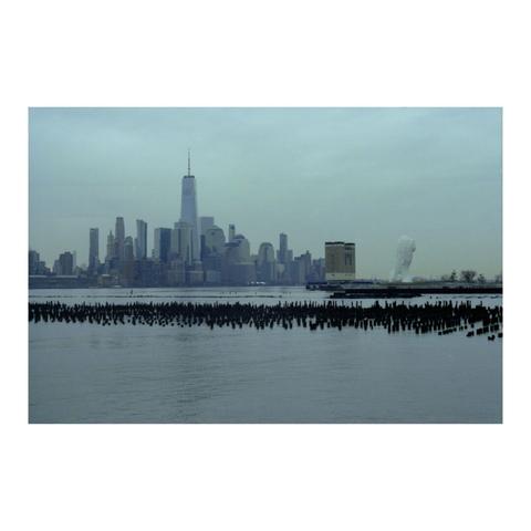 A statue, of a woman holding a finger over her lips, stands overlooking the lower manhattan skyline.