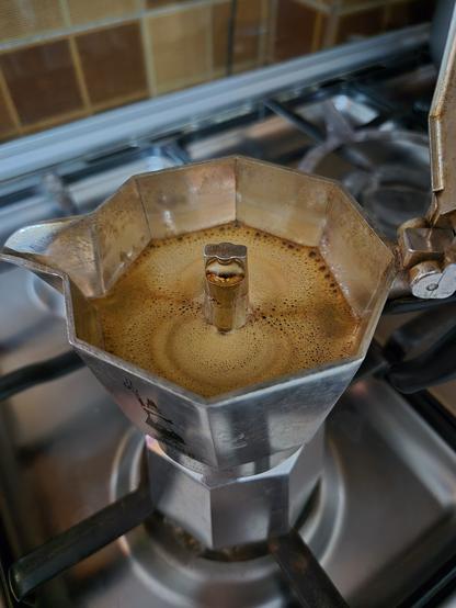 Foamy fresh brew from a moka pot on top of a stove