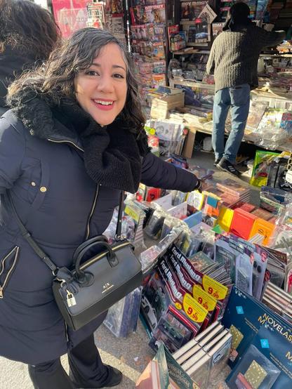 Laura, con un abrigo negro, delante de un kiosko. Señala ilusionada unos ejemplares de Devil May Cry: La acción en 3D sube de nivel