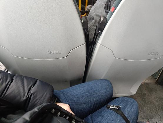 Bilde tatt fra dobbelt bussete som viser to bein, i dongeribukse, som står vinklet kraftig utover siden det ikke er plass til å sitte rett
