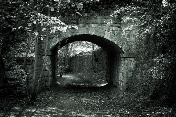 Old stone railways bridge crossing a woodland lane in black and white.