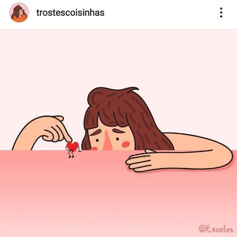 A screenshot of an Instagram post by user trostescoisinhas. It's a 2D illustration of a sad girl leaning on a table, touching a small sad heart-shaped character that is sitting on the table.