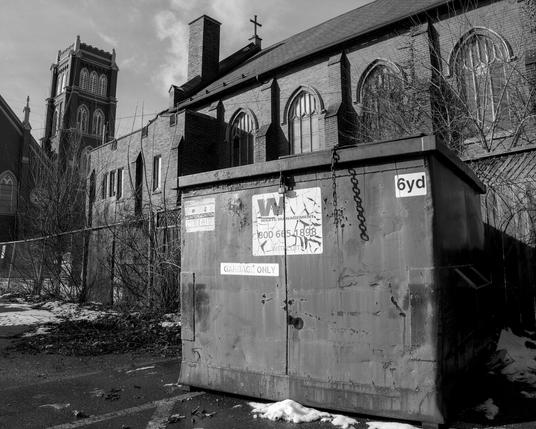 BW low angle outdoor photo of bulk waste bin with upper portions of two churches in background