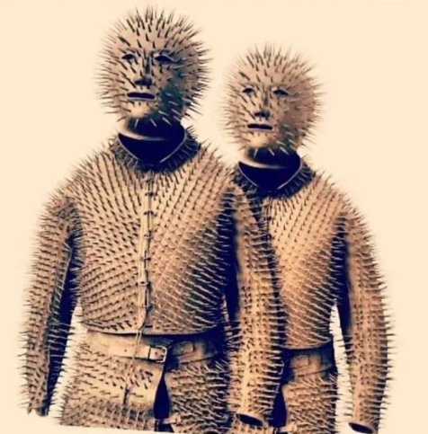 Photograph of two full-body suits and full-head masks are covered in sharp pins.