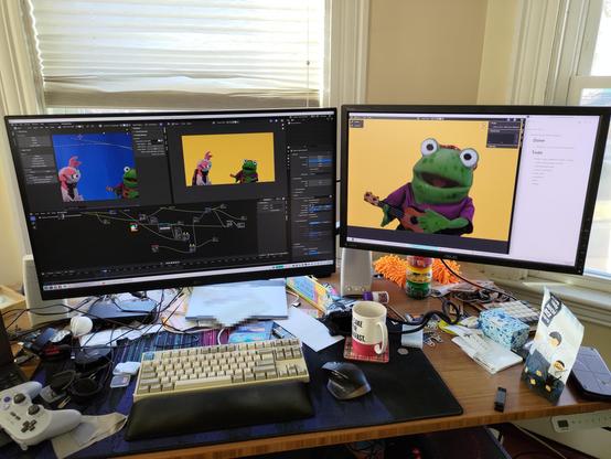 The messy desk where I'm editing my wife's TV Pilot. Two screens side-by-side show my Blender video compositing layout. The previews show the axolotl and frog puppets along with the nodes I'm using to key out the bluescreen.

In front of me on the desk is a whole mess of junk surrounding my beige tenkeyless keyboard with wrist rest.