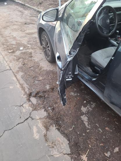 A gray Toyota corolla is parallel parked and its driver's side door is too bent out of shape to open