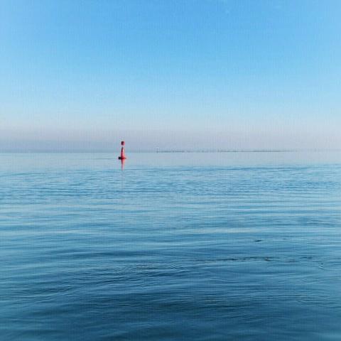 a red buoy on soft blue water against a pale blue sky